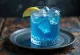 Blue Lagoon kokteilis rotāts ar citrona šķēlīti un kokteiļķirsi